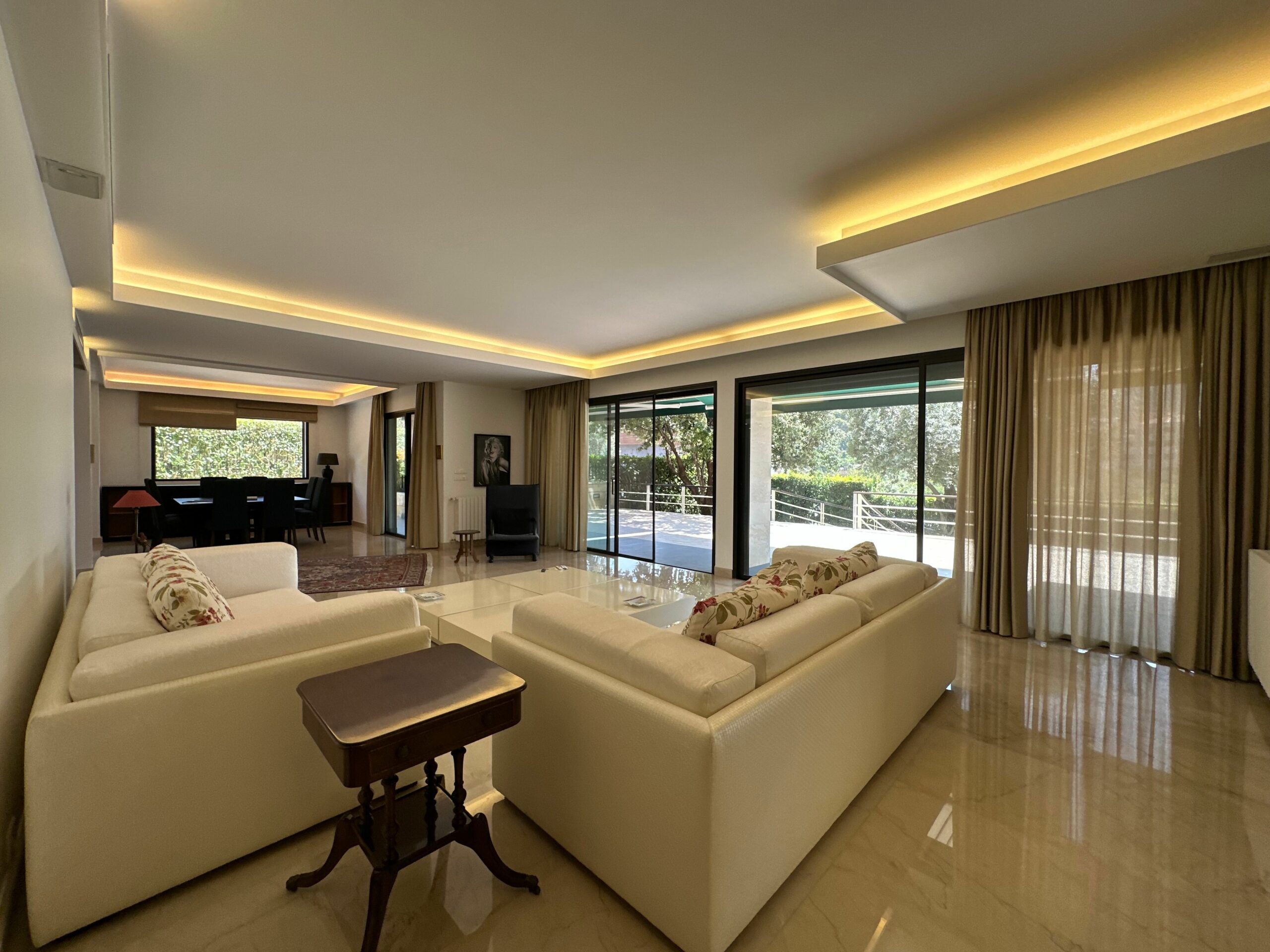 Spacious modern living room featuring large windows, elegant sofas, and warm lighting.